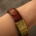 A close-up of a textured brown leather bracelet with geometric embossed patterns and a square antique gold-tone metal clasp, worn on a person's wrist.